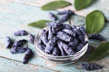 Glass bowl of blue honeysuckle berry on wooden background with copyspace