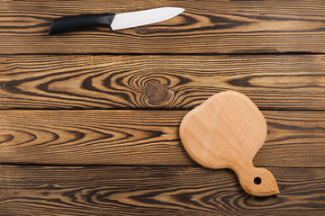 One white ceramic knife with black handle and wooden cutting board on old worn brown table. Top view with copy space