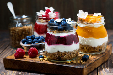 breakfasts in jars with muesli, berry puree and cream on wooden board