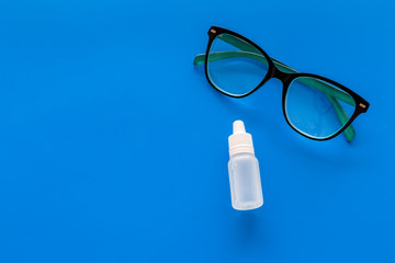 Eye drops in small bottle near glasses on blue background top view copy space