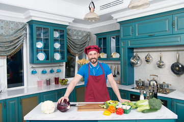 Guy in apron and hat in the kitchen made salad for vegans with lettuce and zucchini. Handsome man preparing vegetables salad at home kitchen. Handsome happy guy prepared all vegetables on the table.