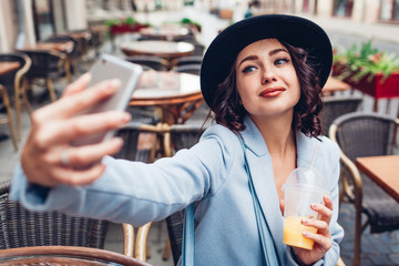 Beautiful young woman taking selfie while having orange juice in outdoor cafe