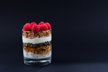 Healthy blueberry and raspberry parfait in a glass on a black background. Two portions. Space for text or design.