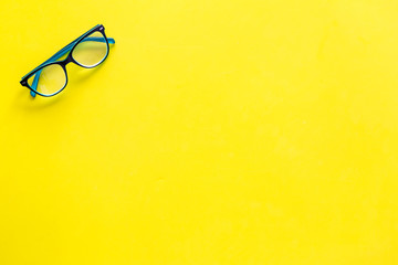 One glasses with transparent lenses on yellow background top view copy space