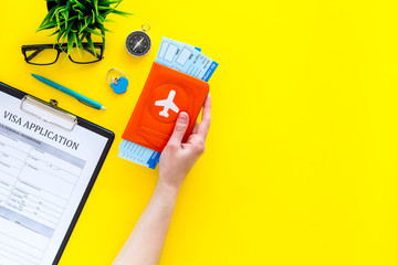 Planning vacation. Visa prosessing. Hand hold airplane tickets in passport cover with airplane silhouette near visa application form, compas on yellow background top view copy space © 9dreamstudio