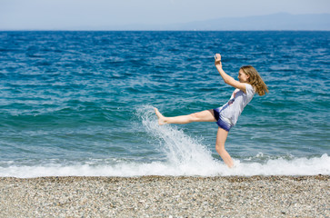 Happy teen enjoys vacation kicking the water at the beach of Sicily 