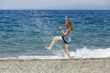 Happy teen enjoys vacation kicking the water at the beach of Sicily 
