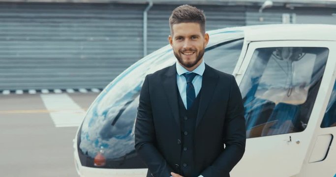 Portrait of young adult businessman executive standing near a private charter helicopter on a helipad. 4K UHD