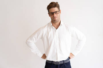 Skeptical handsome man looking at camera and frowning. Guy standing and holding hands on hips. Distrust concept. Isolated front view on white background.