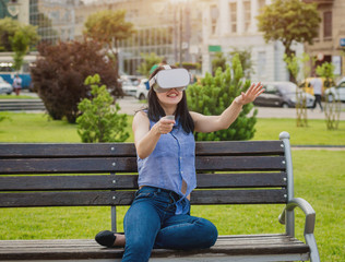 A beautiful young girl plays a game wearing virtual reality glasses on the street.