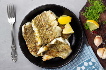Fried cod fish fillet with spice in a cast iron pan. Top view.