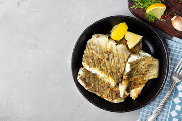 Fried cod fish fillet with spice in a cast iron pan. Top view.