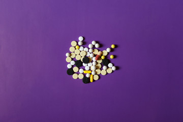 Assorted pharmaceutical medicine pills, tablets and capsules on purple background