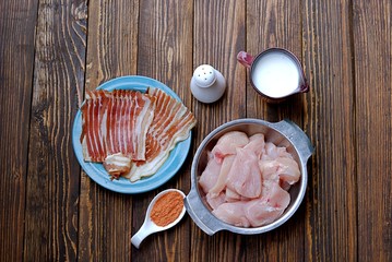 Ignidients for chicken fillet wrapped with smoked bacon, on a wooden background. Raw chicken fillet, buttermilk, spices, smoked bacon, salt.