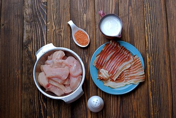 Ignidients for chicken fillet wrapped with smoked bacon, on a wooden background. Raw chicken fillet, buttermilk, spices, smoked bacon, salt.