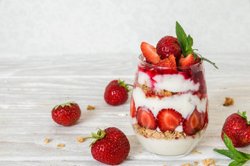 strawberry yogurt parfait with granola, mint and fresh berries in a glass on white wooden table
