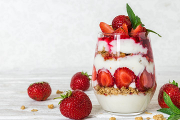 homemade yogurt parfait with granola and strawberry in a glass on white wooden table