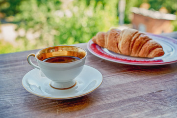 Coffee cup and croissant on wooden table in green garden