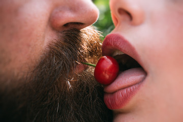 Oral sex. Woman and man play kissing outside. Healthy fruit snack in summer. Concept of two lovers enjoying erotic act with cherry. Provocation and temptation. Bearded man puts cherry in female mouth