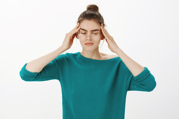 Just a sec, headache again. Portrait of intense gloomy and tired woman in casual outfit and glasses, closing eyes, touching temples and frowning while suffering migraine or painful feeling