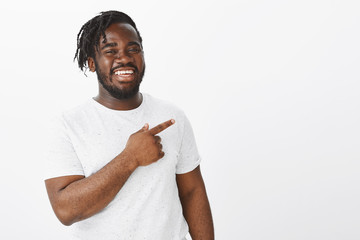 Joyful friendly african-american bearded man in white t-shirt, pointing at upper left corner,...