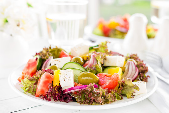 Greek salad. Fresh vegetable salad with tomato, onion, cucumber, pepper, olives, lettuce and feta cheese. Greek salad on plate on white table