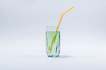 Faceted glass filled with green transparent liquid completed with yellow straw