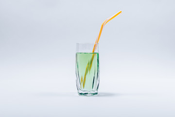 Faceted glass filled with green transparent liquid completed with yellow straw