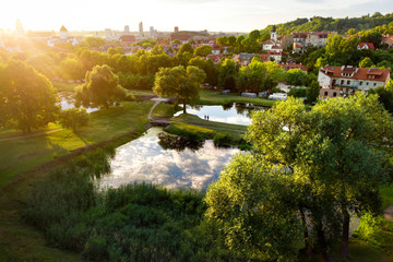 Fototapeta na wymiar Aerial view of Vilnius cityscape shot from Subaciaus viewpoint on sunset. Clouds reflecting in three ponds of Lithuania capital's city park.
