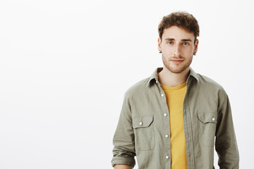 Waist-up shot of charming happy and carefree male coworker in casual clothes standing relaxed over gray background, smirking at camera and gazing with interest, taking part in conversation