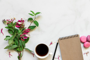 creative layout made of honeysuckle flowers bouquet, coffee cup, blank notebook and macaroons