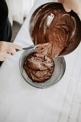 Chocolate cake dough being transferred into round-shaped baking tin with silicone spatula. Woman preparing chocolate cake to be baked. White background.