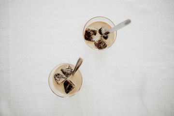 Frozen coffee ice cubes in two glasses poured with milk to make a refreshing summer iced coffee drink. White background, view from above, isolated, copy space.