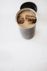 Iced coffee to go. Frozen coffee ice cubes in a vacuum flask poured with milk. Thermos lid near the bottle. White background. Isolated, copy space.