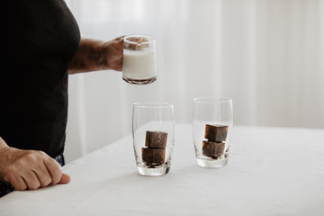 Woman preparing iced coffee. Frozen coffee ice cubes in a glass poured with milk to make a refreshing summer drink. White background. Body parts.