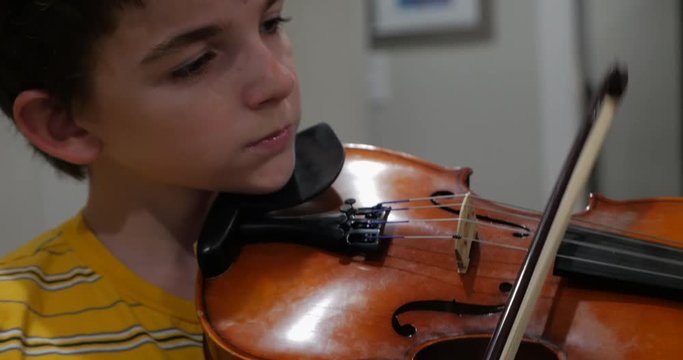 Young male child prodigy focusing and playing violin in his home