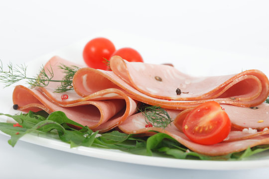 Portion of sliced Mortadella with green herbs on white plate. Bologna salami on white background.