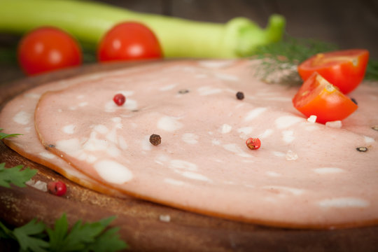 Italian mortadella salami on wooden board with tomato and green pepper