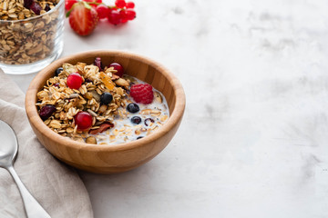 Healthy breakfast in a bowl with homemade baked granola,fresh berries, fresh strawberries and milk on a white table. Copy space.