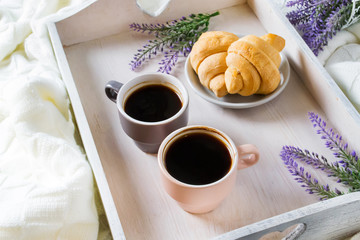 Croissants and coffee on a wooden white tray with lavender flowers in bed. Romantic breakfast