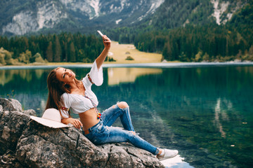 Young happy woman doing selfie on a rock by the lake