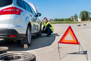 Woman driver changing damaged wheel on roadside