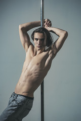 Young strong sexy pole dance man on grey background.