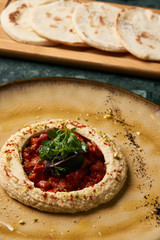 Delicious Hummus with harissa sauce and pistachios, close-up. Vegetarian diet food with pita bread on wooden cutting board