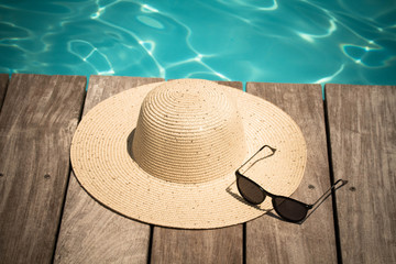 chapeau et lunettes au bord d'une piscine - obrazy, fototapety, plakaty