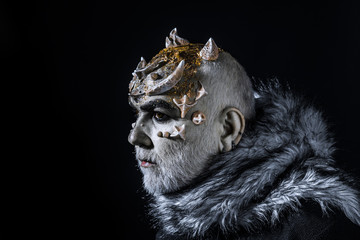 Alien, demon, sorcerer makeup. Demon on black background, copy space. Theatrical makeup concept. Senior man with white beard dressed like monster. Man with thorns or warts in fur coat
