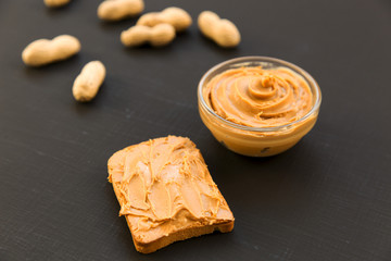 Bowl of peanut butter, unshelled peanuts on a black background, side view.
