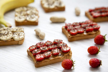 Vegetarian toasts with peanut butter, fruits and chia seeds on a white wooden table, side view. Some ingredients. Dieting concept. Close-up.