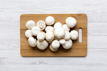 Champignon mushrooms on bamboo board over white wooden surface, top view. From above, overhead.