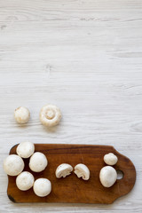 Champignon mushrooms on rustic wooden board over white wooden background, top view. From above. Copy space.